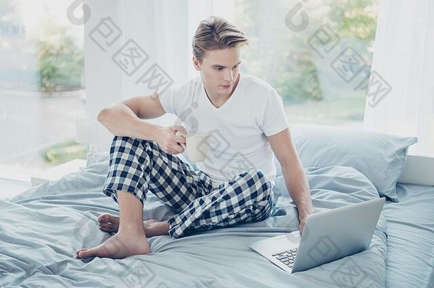 浓密金发男子的全尺寸照片使用笔记本电脑进行<strong>工作制</strong>作项目他的老板想要拿咖啡杯坐在床上穿格子花呢