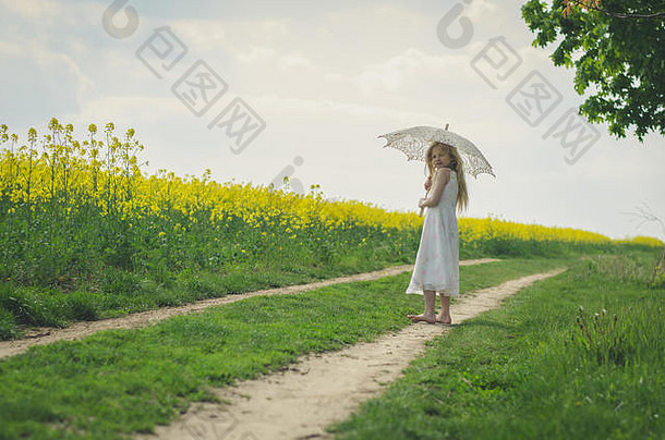 可爱的金发孩子在乡村小路上用白色蕾丝雨伞保护自己免受阳光的伤害
