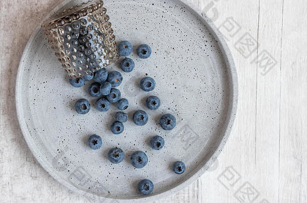 蓝莓放在一个<strong>玻璃</strong>碗里，散落在一个灰色盘子上。顶视图。空间。