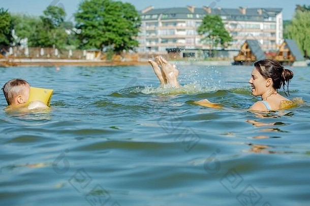 带着充气臂章的蹒跚学步的小男孩和妈妈在湖水里玩耍