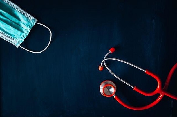 黑色黑板上的红色听诊器和白色医用外科口罩，黑色文本编辑空间。黑色编辑空间。冠状病毒防护概念图