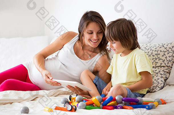 可爱的怀<strong>孕妈妈</strong>和小男孩在家里玩玩具，在平板电脑上看电影