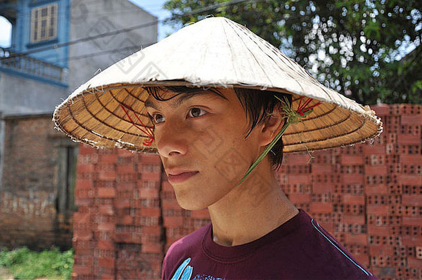 在越南，一名少年游客戴着一顶圆锥形帽子以躲避阳光