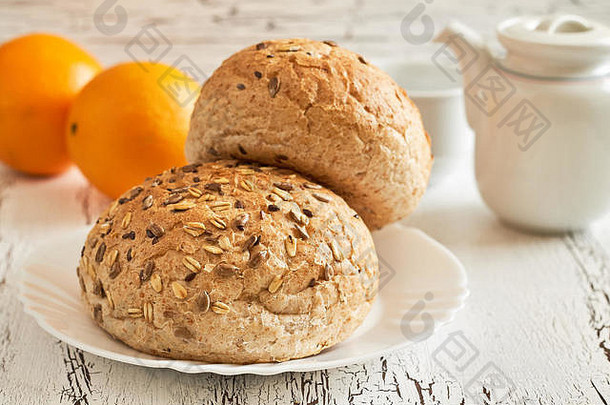 白色乡村餐桌上的全麦面包，配以茶壶和橙子的混合种子。健康早餐概念图