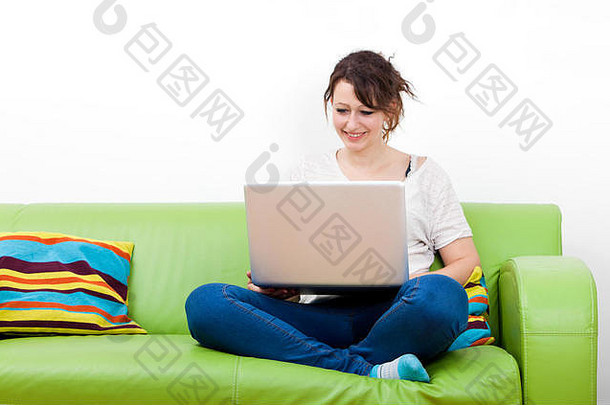 坐在绿色沙发上使用笔记本电脑的快乐年轻女子的全长