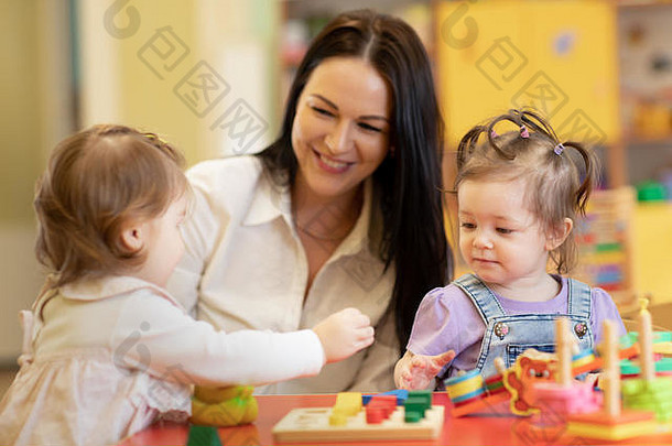 可爱的女人和微笑的孩子在幼儿园或托儿所玩教育玩具
