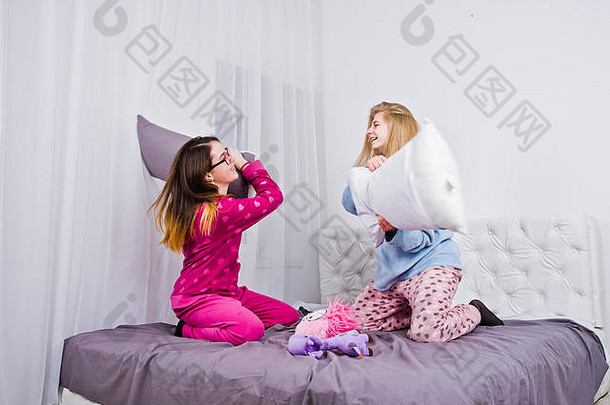 两个穿着睡衣的女孩在房间的床上玩得很开心。