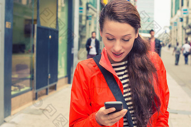 美丽的年轻女子走在城市的街道上，用她的手机