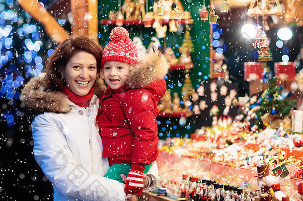 戴着暖帽的母亲和孩子在传统的德国圣诞街市场观看手工制作的玻璃圣诞树装饰品。带孩子的家庭为孩子购物