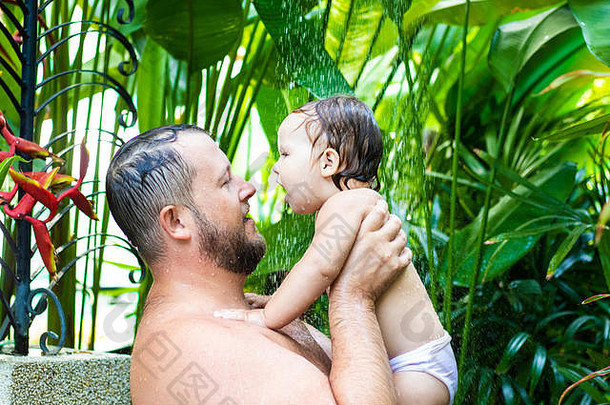 爸爸和宝宝在热带阵雨下。爸爸和宝宝在沙滩上沐浴着水花嬉戏