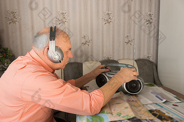 老人坐在家里的桌子旁，戴着耳机听收音机。