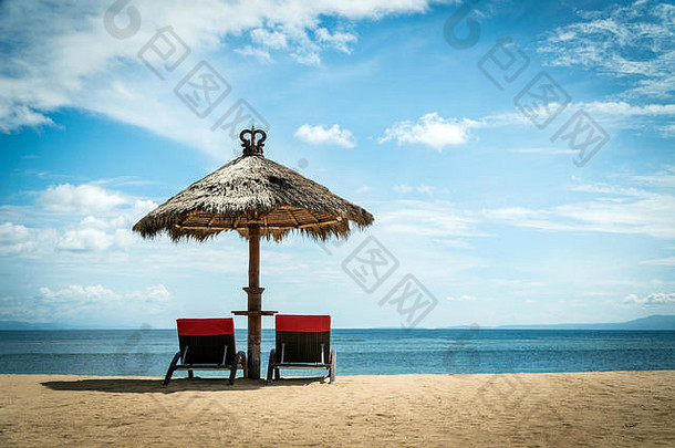 海岸上柳条伞下的两把红色沙滩椅。田园度<strong>假景观</strong>概念