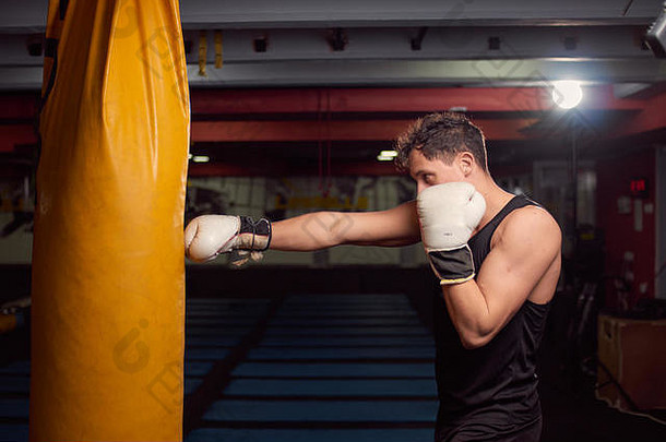 一名年轻男子，拳击手手击打拳击袋，在室内健身房练习，戴拳击手套，上身射击。