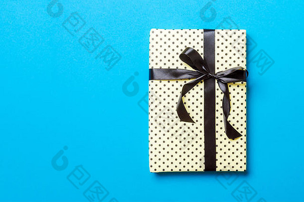 用蓝色背景上的黑色丝带用纸包装的圣诞或其他节日手工礼品。礼品盒，彩台礼品装饰，t