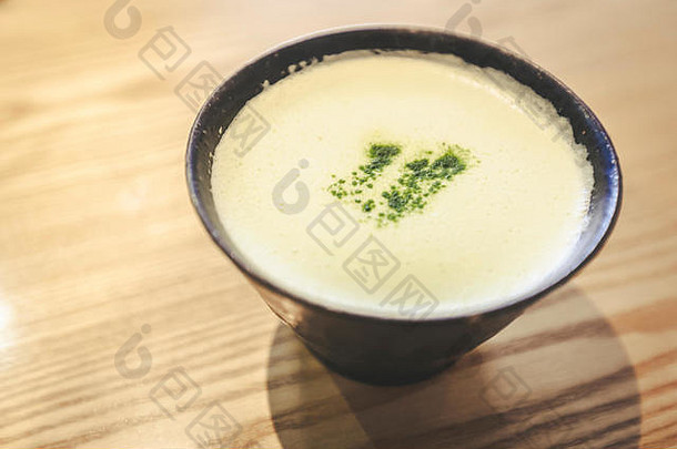 新鲜酿造的抹茶拿铁咖啡的特写镜头，配有日本抹茶绿茶粉、红杯和时尚的木桌
