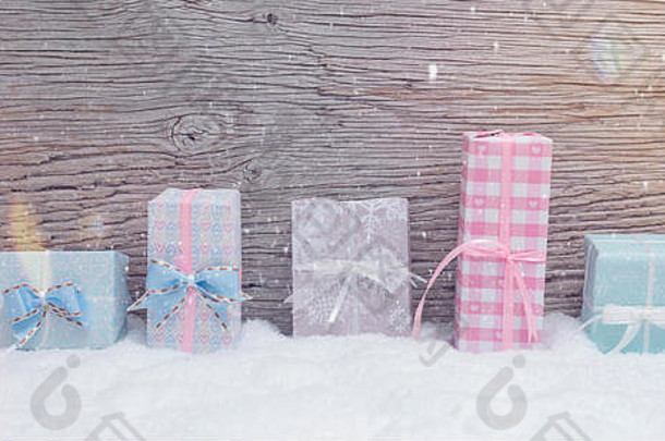 5件小圣诞礼物放在雪地里的彩色精美包装纸里。带有降雪和镜头光斑的木质背景。