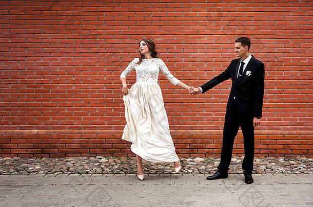 新婚夫妇拥抱红色的砖墙年轻的婚礼夫妇