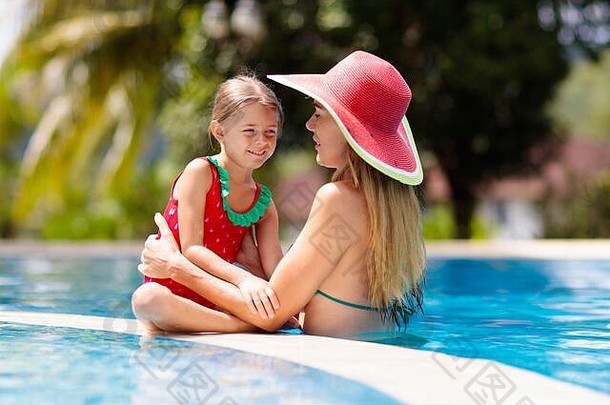 母亲和孩子在游泳池里。妈妈和孩子在热带度假村游泳。夏日海滩度假时，穿着红色泳衣、戴着帽子的年轻女子和小女孩。