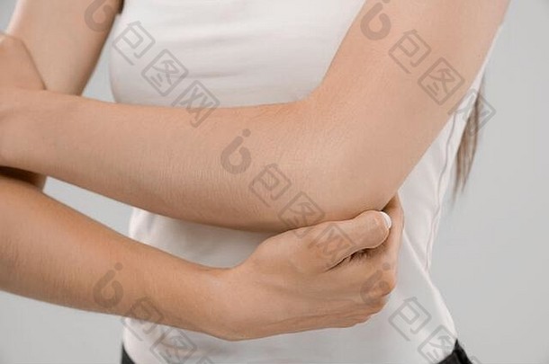 一名身穿白衬衫的不知名白人妇女在灰色隔离背景上摆姿势，因受伤而触摸肘部。手臂疼痛的黑发女人的前腰。