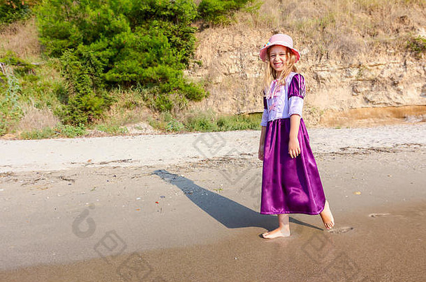 年轻的女人，戴着帽子的孩子，穿着可爱的夏装，在浅水中的海边散步。
