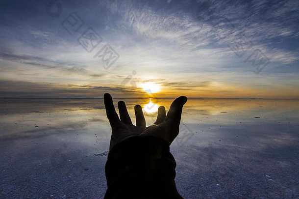 在这个神奇的地球上，伸出希望之手。试图在乌尤尼盐滩捕捉阳光，这是一幅田园诗般的彩色风景，倒映在水中