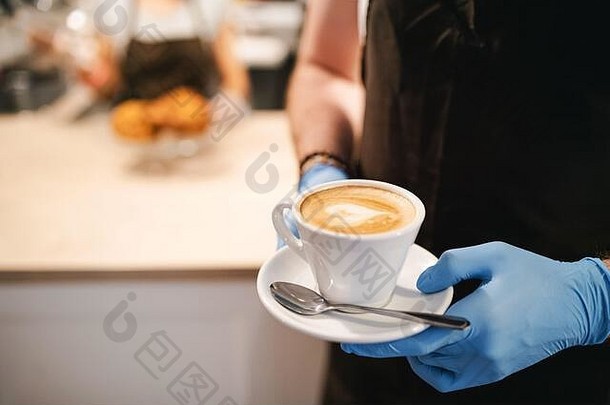 面目全非的女服务员戴着手套在咖啡馆里工作，手里拿着一杯咖啡。