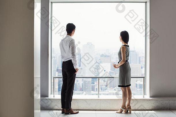 站在一扇可以俯瞰<strong>城市</strong>的大窗户旁的商人和女商人。