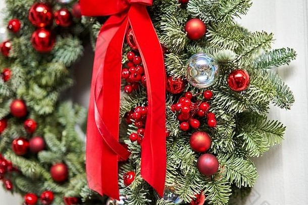 白色的门上挂着美丽的红色圣诞花环，上面缀着新鲜的云杉。房子的入口。圣诞节的气氛。圣诞树。