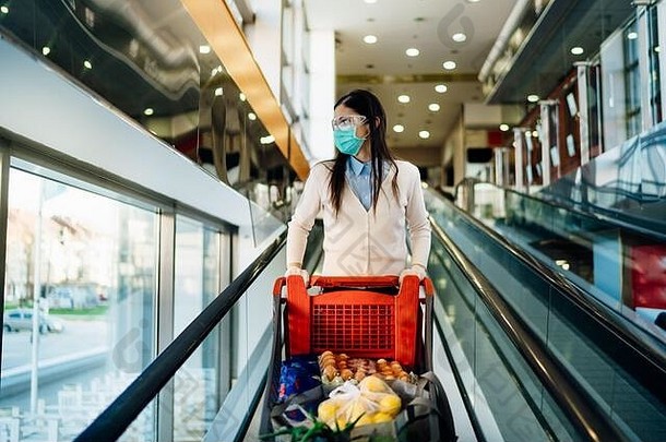 戴面具的女人在超市购物，推着购物车。食品抢购和囤积。2019冠状病毒疾病携带者购物车。Sus