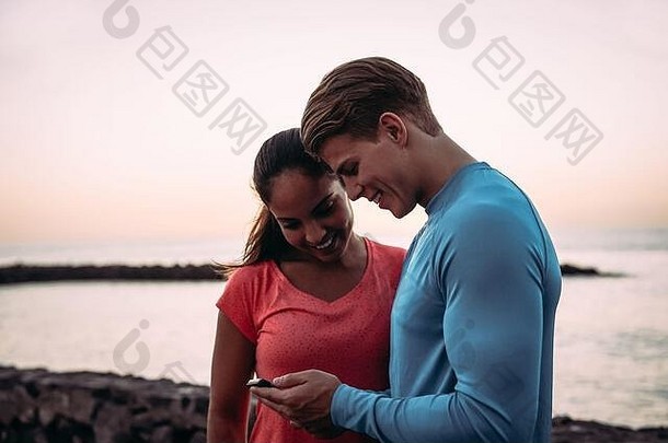 一对年轻的夫妇在户外慢跑并使用移动智能手机——运动型的人在手机上享受潮流科技应用的乐趣