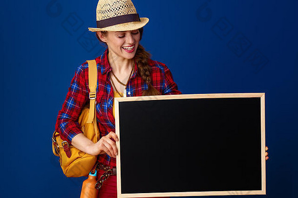 寻找鼓舞人心的地方。带着背包的微笑健康的女游客在蓝色背景下看着白板