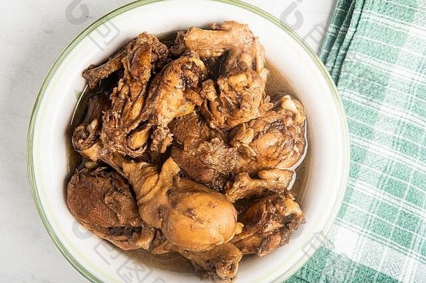 一份菲律宾风格的鸡肉阿多波菜，盛在碗里，绿色餐巾放在大理石桌面上。