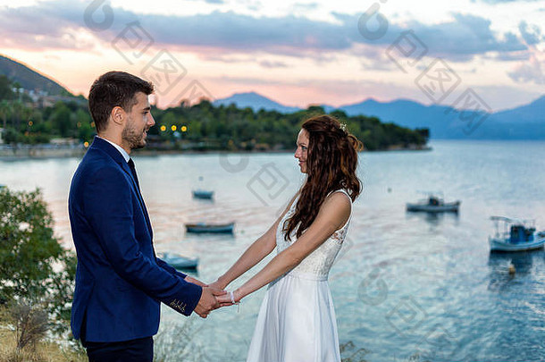 年轻的新娘和新郎手牵手在悬崖上，可以看到美丽的海景。