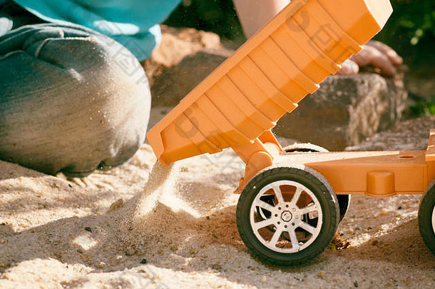 一个孩子在沙滩上玩大玩具车、挖掘机和卡车