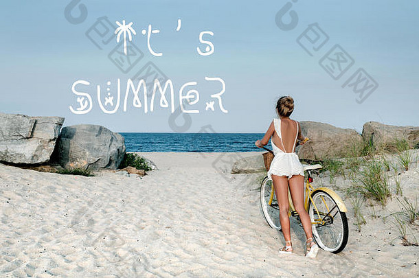 海滩上骑自行车的美女。带字母的海洋背景现在是夏天