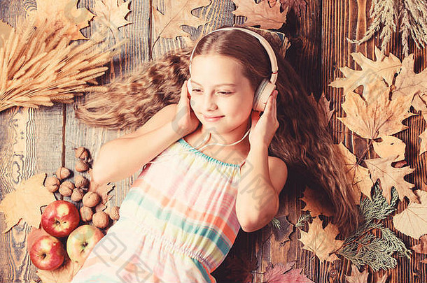 进入秋天的情绪。以秋天为背景的可爱的音乐迷。戴着耳机听音乐的小女孩。戴着立体声耳机的小女孩。可爱的孩子喜欢用耳机播放音乐。