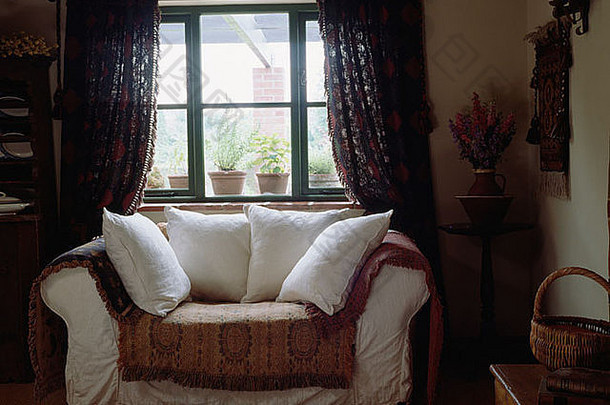 在小屋客厅里，白色沙发上有白色靠垫，窗前有图案的沙发