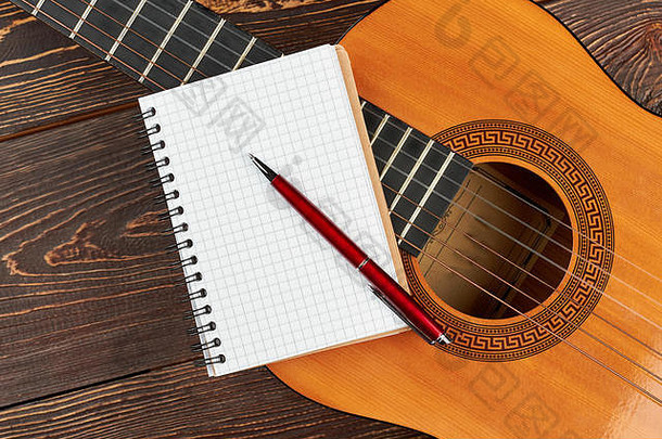 吉他上的空白笔记本和钢笔。