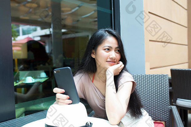 美丽的亚洲女人高高兴兴地坐在咖啡馆里，手里拿着智能手机