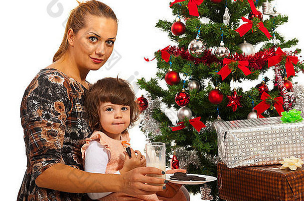 妈妈和女儿坐在圣诞树旁，手里拿着牛奶和饼干