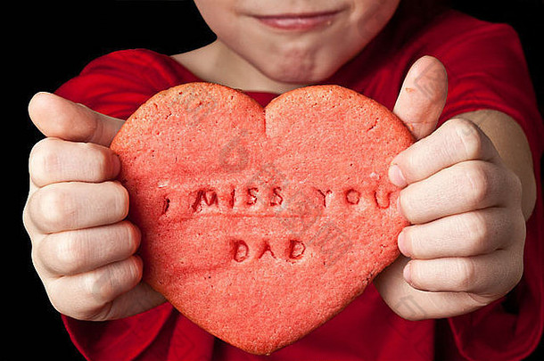 小男孩手里拿着红色心形饼干，上面写着“我想<strong>你</strong>，爸爸”