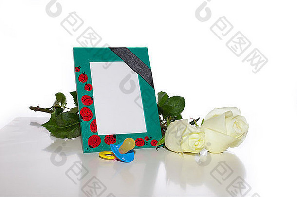 托儿所里有一个相框，相框上有一条黑色的吊带，白色的玫瑰和一个儿童假人