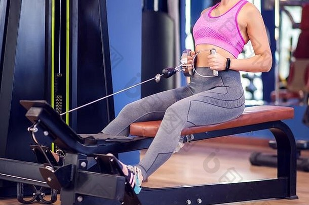 一位身穿粉色上衣、金色短发的女士在健身房锻炼背部<strong>肌肉</strong>。人、健康和保健概念