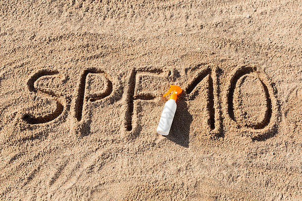防晒系数十。SPF 10字写在沙子上，白色的瓶子上涂有防晒霜。皮肤护理概念背景。