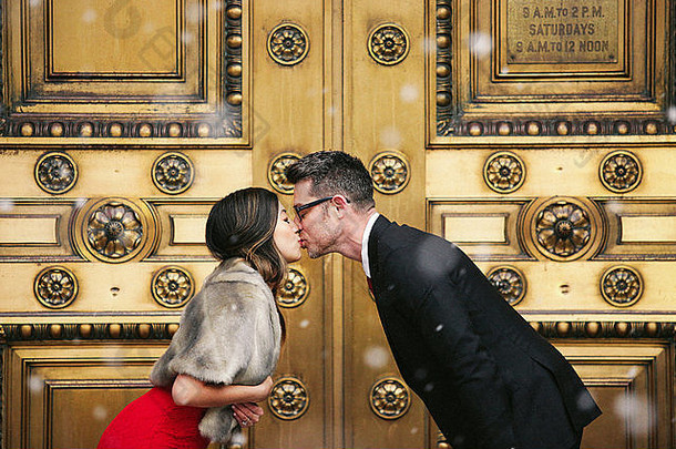 一对夫妇，一男一女在一座<strong>城市</strong>建筑装饰的大门前接吻。