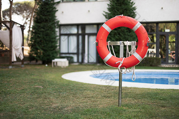 一个橙色和白色橡胶救生浮子的特写照片，站在一个游泳池的安全地带，用绳子