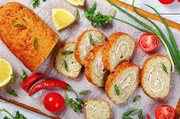 特写镜头：美味的烤箱烤鱼切碎的白鱼片卷在案板上切成片，配以葱、新鲜的欧芹、柠檬