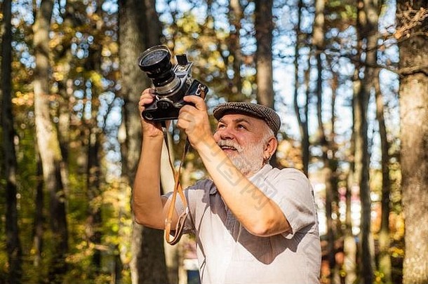 最好的专业相机。秋日的老<strong>摄影</strong>师。老金的人在森林里拿着老式相机。拿着照相机的老人。使用模拟摄像机进行拍摄。自然<strong>摄影课</strong>。