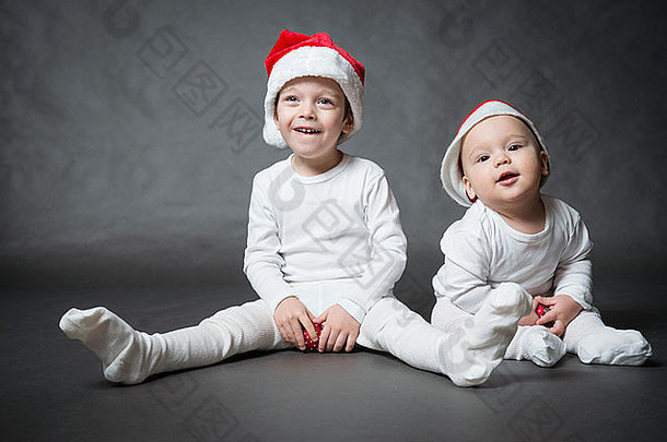 两个戴圣诞帽的可爱男孩的肖像，灰色背景