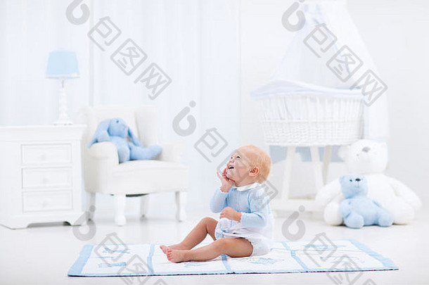 可爱的婴儿男孩玩蓝色的地板上席喝牛奶瓶白色阳光明媚的托儿所摇摆椅子